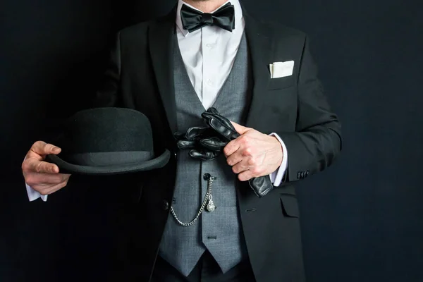 Portrait of Man in Dark Suit Holding Bowler Hat and Leather Gloves. Concept of Classic English Gentleman. Retro Style and Vintage Fashion.