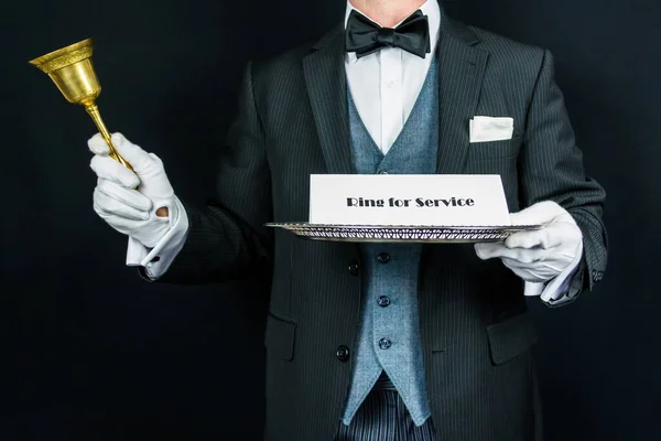 Portrait of Butler in Dark Formal Attire and White Gloves Holding Gold Bell and Sign on Silver Tray. Ring for Service. Concept of Professional Courtesy.