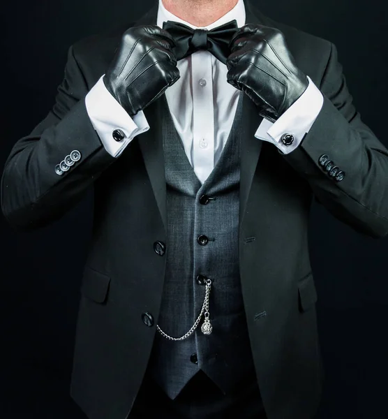 Portrait of Man in Dark Formal Attire and Leather Gloves Straightening His Bow Tie. Vintage Style and Retro Fashion.
