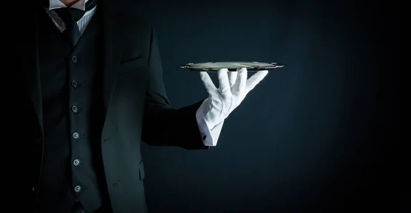 Portrait of Butler in Formal Attire and White Gloves Holding Silver Serving Tray on Black Background. Copy Space for Service Industry and Professional Hospitality