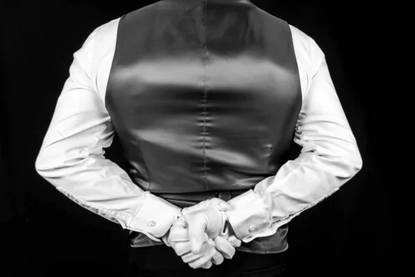 Butler or Waiter Standing with Hands Behind Back on Black Background. Concept of Service Industry and Professional Hospitality. Formal White Glove Service.