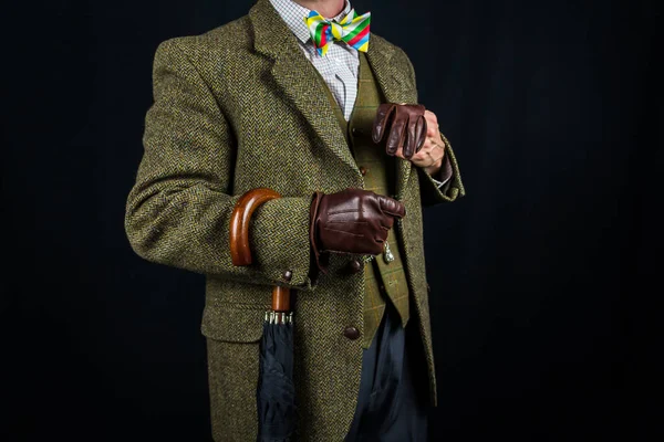 Gentleman in Tweed Suit and Leather Gloves with Umbrella on Arm on Black Background. Concept of Classic and Eccentric British Gentleman