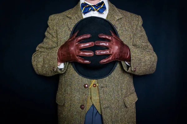 Portrait of Man in Tweed Suit and Leather Gloves Holding Bowler Hat on Black Background. Classic and Eccentric English Gentleman.