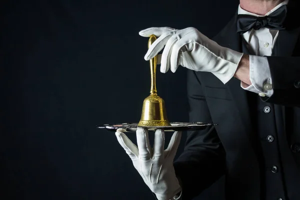 Portrait of Butler in White Gloves and Dark Suit Holding Gold Bell on Silver Tray. Copy Space for Service Industry and Professional Hospitality.