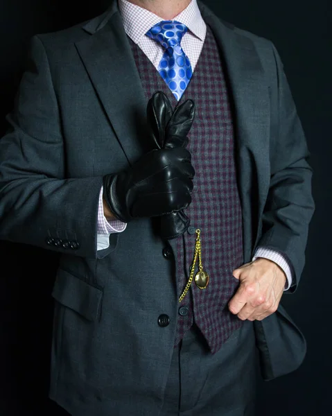 Portrait of Gentleman in Gray Suit on Black Background Holding Leather Gloves. Vintage Style and Retro Fashion.