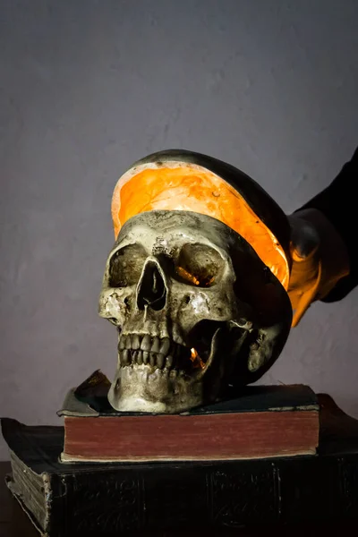 Portrait of Mysterious Figure Lifting the Top of a Human Skull on Stack of Ancient Books. Light After Death. Dark and Haunting.