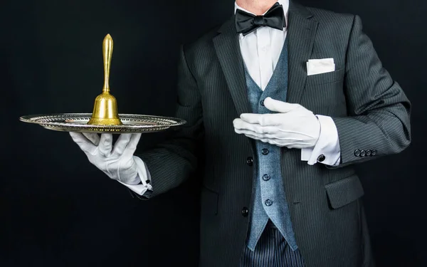 Portrait of Butler in Dark Formal Suit and White Gloves Holding Gold Bell on Silver Tray. Concept of Service Industry and Professional Hospitality.