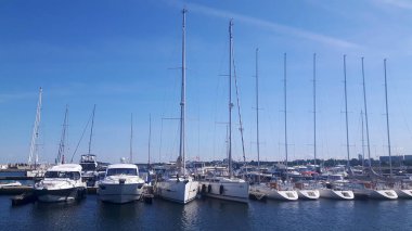 The photo shows several sailboats docked in a marina. Calm water and a clear sky create an atmosphere of relaxation and maritime harmony