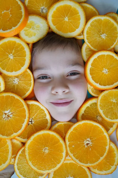 Close up male model face in the middle sliced oranges. Portrait of beautiful teenager among sliced oranges. Orange frame. Healthy food concept and summer time. Close-up view from above