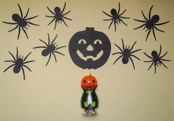 Cute character in monster costume. Scary Halloween figurine stand on a light background close-up, behind hangs terrible black pumpkin and spiders. Halloween concept. Holiday decorations
