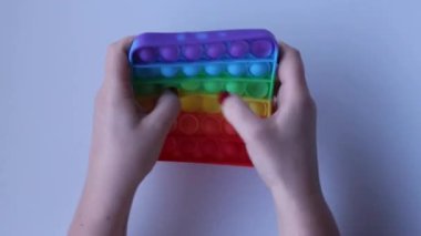 Womens hands with a beautiful manicure crumple a square rubber soothing toy and evil abandons her. Pop It close-up top view. Board game for development of motor skills. Popit gamer. Antistress toy