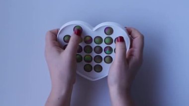 Women hands crumple and play with large heart Pop It close-up top view. Board game for the development of motor skills. Trendy toy Big Pop It fidget. Popit gamer. Antistress toy