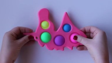 Women hands crumple and play with pink Pop It Unicorn close-up top view. Board game for the development of motor skills. Christmas concept. Popit gamer. Antistress toy. Pressing bubbles
