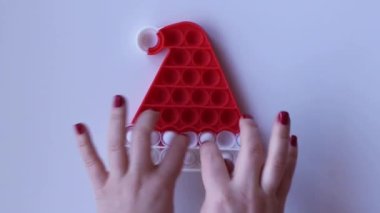 Women hands crumple and play with large Pop It Christmas hat close-up top view. Board game for the development of motor skills. Christmas concept. Popit gamer. New antistress toy. Pressing bubbles