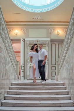 Bride and groom in wedding costumes stand on the stairs in the wedding palace. Wedding photo