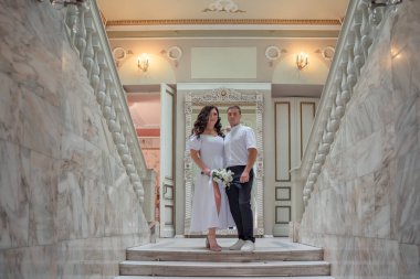 Bride and groom in wedding costumes stand on the stairs in the wedding palace. Wedding photo.