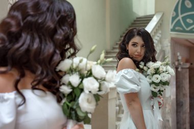 A beautiful bride with curly black hair in a white wedding dress with lace sleeves and a bouquet