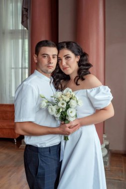 Happy new family. The bride gently snuggled up to the groom. Happy bride and groom. Portrait of a man and a woman in a white vintage dress in a classic interior on a wedding day. Wedding day