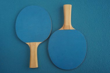 Two blue table tennis rackets lie upside down on a blue background with a close-up view from above. Game for leisure. Sport equipment. International competition. Selective focus, blurred background