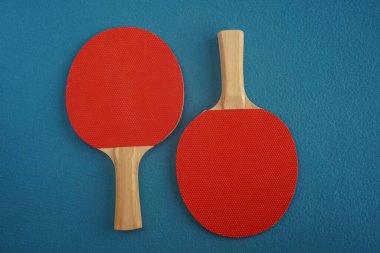 Two red table tennis rackets lie upside down on a blue background with a close-up view from above. Game for leisure. Sport equipment. International competition. Table tennis. Healthy lifestyle