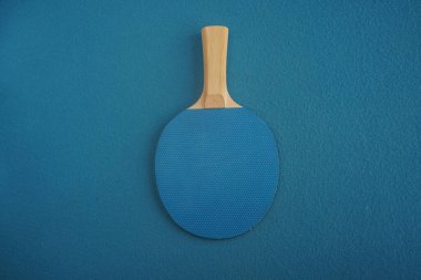 Blue table tennis or ping pong racket lies upside down on blue background with a close-up view from above. Game for leisure. Sport equipment.