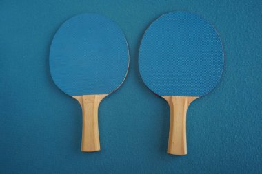 Two blue table tennis or ping pong rackets lie on a blue background with a close-up view from above. Game for leisure. Sport equipment. International competition. Table tennis. Healthy lifestyle