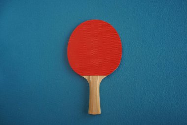 Red table tennis or ping pong racket lie on a blue background with a close-up view from above. Game for leisure. Sport equipment. International competition. Table tennis. Healthy lifestyle