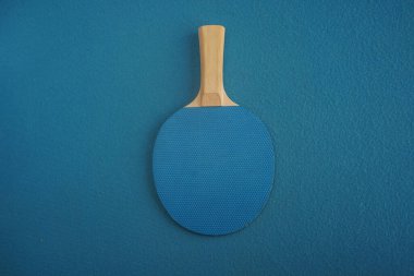 Blue table tennis racket lies upside down on blue velvet background with a close-up view from above. Game for leisure. Sport equipment.