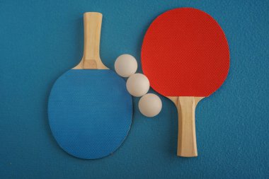 Red and blue table tennis or ping pong rackets and three balls lie on a blue background with a close-up view from above. Game for leisure. Sport equipment. International competition. Healthy lifestyle
