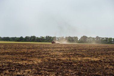 A tractor is plowing a field in the dust. Harvesting with a combine. The tractor is cultivating the field. Red tractor in the dust. Tractor on the field. Selective focus, blurred background