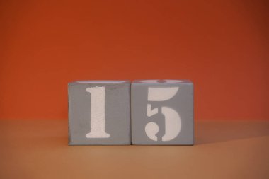 Number 15 on wooden grey cubes close-up. Concept of date time. Math concept. Copy space for text or event. White numbers 15 on building blocks, orange background. Educational cubes. Selective focus