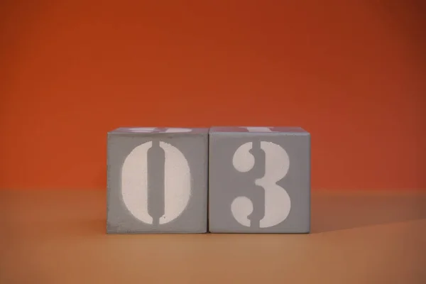 Number 03 on wooden grey cubes close-up. Concept of date time. Math concept. Copy space for text or event. White numbers 3 on building blocks, orange background. Educational cubes. Selective focus