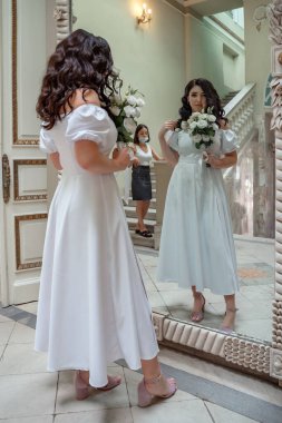 A beautiful bride with curly black hair in a white wedding dress with lace sleeves and a bouquet of white flowers
