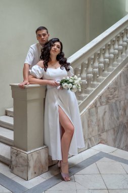 Lush, charming bride on the stairs. Stylish girl in wedding dress with bridal bouquet.