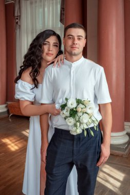 Serious newlyweds. Happy new family. The bride gently snuggled up to the groom. Happy bride and groom. Portrait of a man and a woman in a white vintage dress in a classic interior on a wedding day.