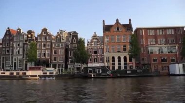 Amsterdam, view of city from river, camera floats under bridge. Traditional Dutch-style urban buildings in summer from river. Amsterdam city skyline sunset at canal waterfront. Tourism