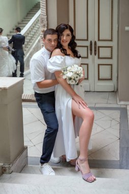 Beautiful caucasian newlywed couple in white dress with a bouquet of white peonies hugging and admiring. Attractive bride and groom portrait.