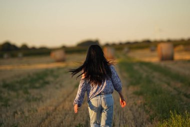The girl runs across the field, the view from behind, her long black hair flying in the wind, a young woman in jeans and a light blouse in nature. A healthy diet and a pesticide-free harvest are the key to a healthy life