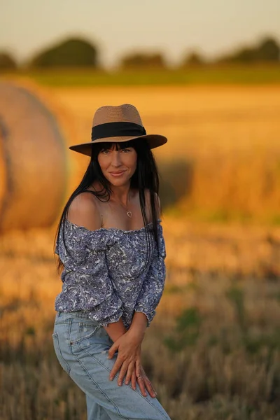 A model in a hat in nature demonstrates smooth fresh skin of the hands and bare shoulders, a woman with long silky hair, natural skin and hair care