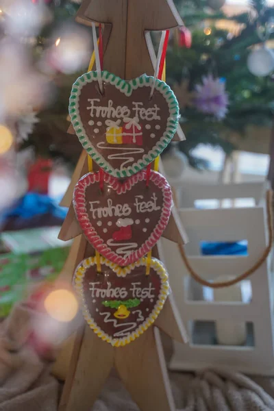 Christmas food. Colorful Christmas handmade gingerbread in the shape of heart hangs on wooden tree close-up. Behind Christmas decor. Christmas cozy atmosphere. Selective focus