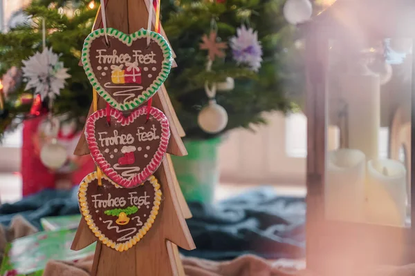 Christmas food. Colorful Christmas handmade gingerbread in the shape of heart hangs on wooden tree close-up. Behind Santa. Bokeh effect. Selective focus