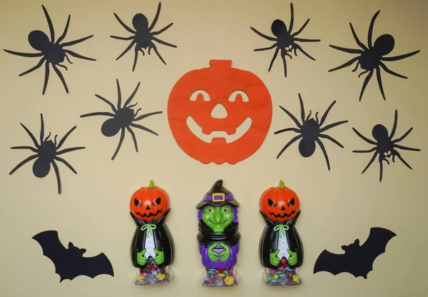 Scary Halloween figurines stand on a light background in close-up, behind hangs terrible pumpkin and spiders. Cute character in monster costume. Halloween concept. Holiday decorations toys