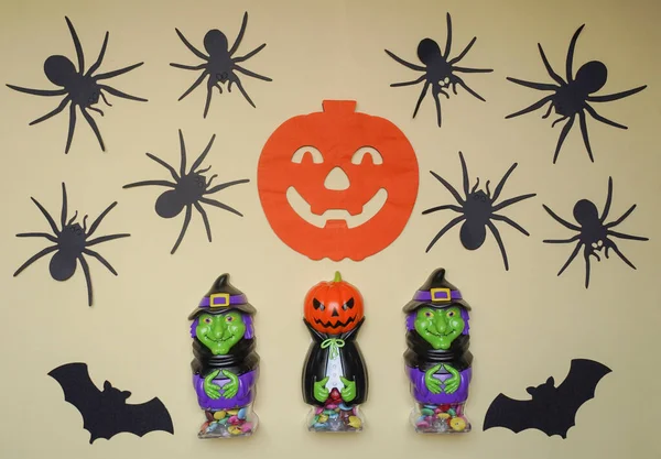 Scary Halloween figurines stand on a light background in close-up, behind hangs terrible pumpkin, spiders and bats. Cute character in monster costume. Halloween concept