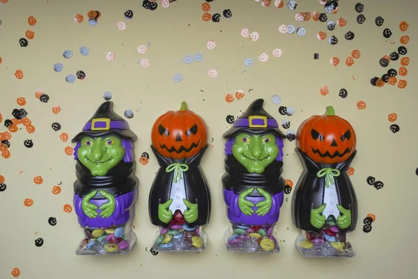 Terrible figures of witches and monsters on a light background strewn with colorful confetti. The concept of the Halloween holiday. Festive figurines.