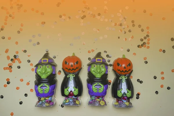 Terrible figures of witches and monsters on a light background strewn with colorful confetti. The concept of the terrible Halloween holiday. Festive figurines. Halloween days