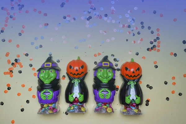 Terrible figures of witches and monsters on a light background strewn with colorful confetti. The concept of the terrible Halloween holiday. Festive figurines.