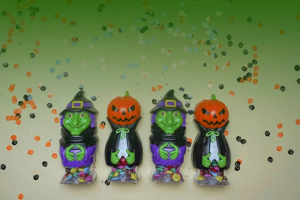 Terrible figures of witches and monsters on a light background strewn with colorful confetti. The concept of the terrible Halloween holiday. Festive figurines. Empty space. Halloween decorations