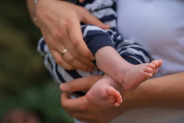Mother\'s hands keep the baby\'s feet close-up. Bare legs of a child. Maternal tenderness. Taking care of an infant. An innocent child. Selective focus. Modern Pediatrics