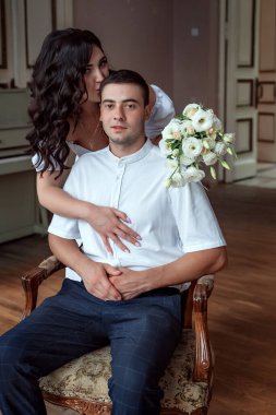 Portrait of the seated groom and behind him embraced by a black-haired bride
