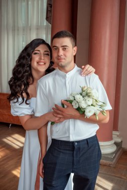 Happy newlyweds. Happy new family. The bride gently snuggled up to the groom. Happy bride and groom. Portrait of a man and a woman in a white vintage dress in a classic interior on a wedding day.